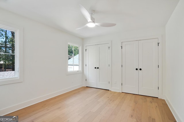 unfurnished bedroom featuring light wood finished floors, a ceiling fan, baseboards, and two closets