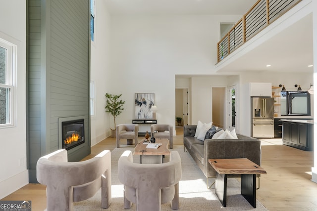 living room with a towering ceiling, light hardwood / wood-style floors, and a large fireplace