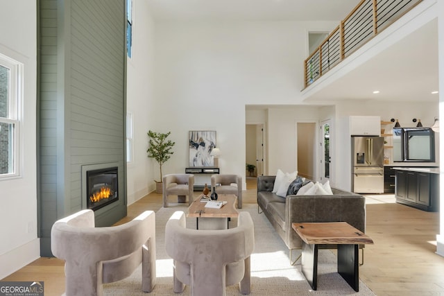 living room featuring light wood-type flooring, a large fireplace, a high ceiling, and baseboards