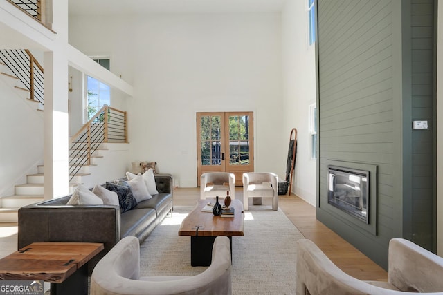 living room with a large fireplace, stairs, light wood-style flooring, french doors, and a towering ceiling