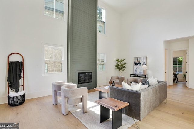 living room with light wood finished floors, a large fireplace, a wealth of natural light, and a towering ceiling