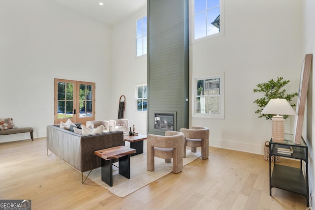 living area with light wood finished floors, a fireplace, baseboards, and french doors