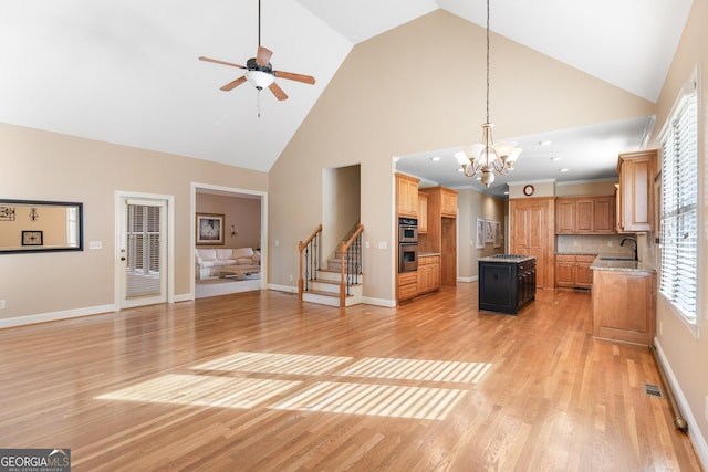 unfurnished living room featuring sink, high vaulted ceiling, light hardwood / wood-style floors, and ceiling fan with notable chandelier