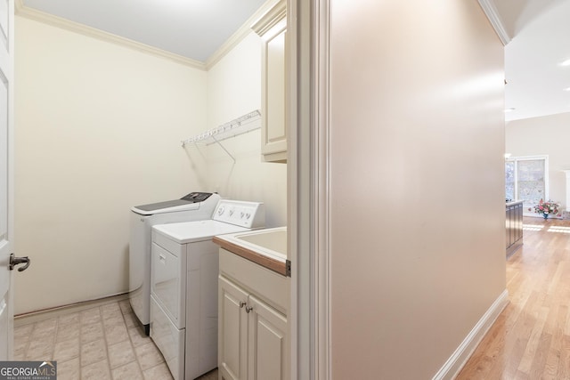 laundry room with cabinets, light wood-type flooring, crown molding, and washing machine and clothes dryer