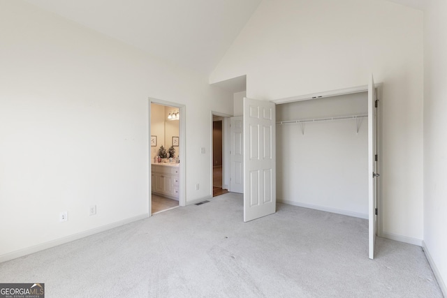 unfurnished bedroom with high vaulted ceiling, light colored carpet, connected bathroom, and a closet