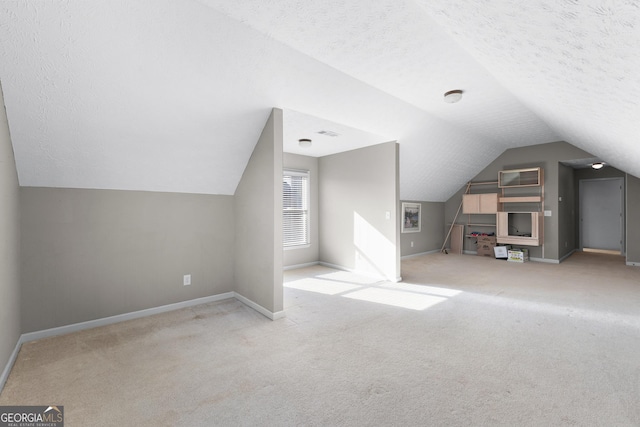 additional living space featuring light carpet, a textured ceiling, and vaulted ceiling