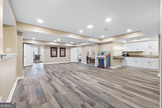 unfurnished living room featuring sink, a tray ceiling, and light hardwood / wood-style flooring