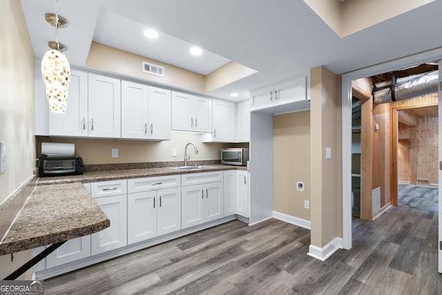 kitchen with dark wood-type flooring, sink, white cabinets, and hanging light fixtures