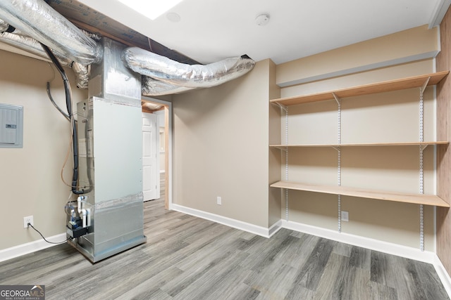 basement featuring hardwood / wood-style flooring, electric panel, and heating unit