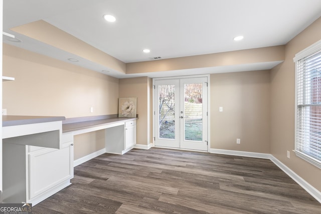 unfurnished office with built in desk, dark wood-type flooring, and french doors