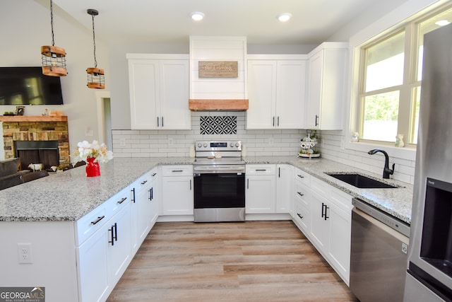 kitchen with light hardwood / wood-style flooring, stainless steel appliances, sink, a stone fireplace, and tasteful backsplash