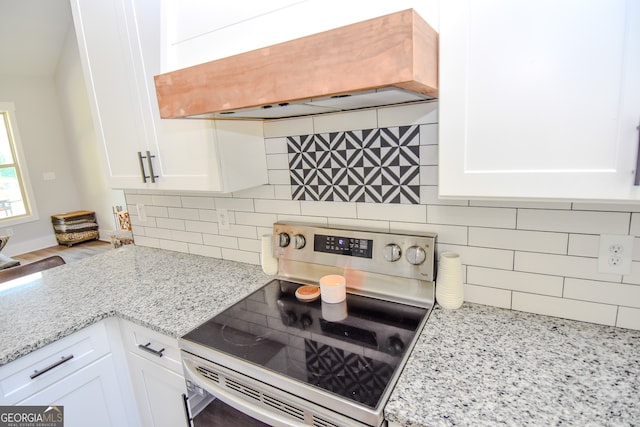 kitchen with stainless steel electric range, backsplash, light stone counters, white cabinetry, and premium range hood