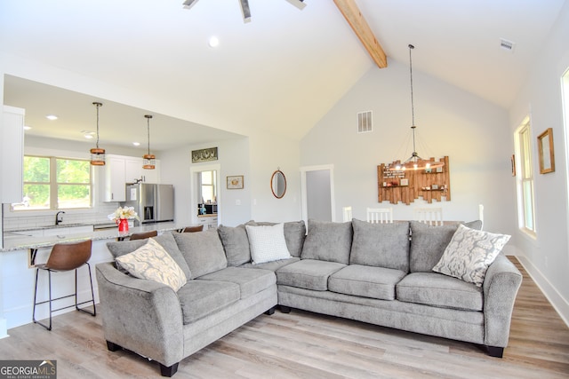 living room with light wood-type flooring, high vaulted ceiling, a notable chandelier, and beamed ceiling