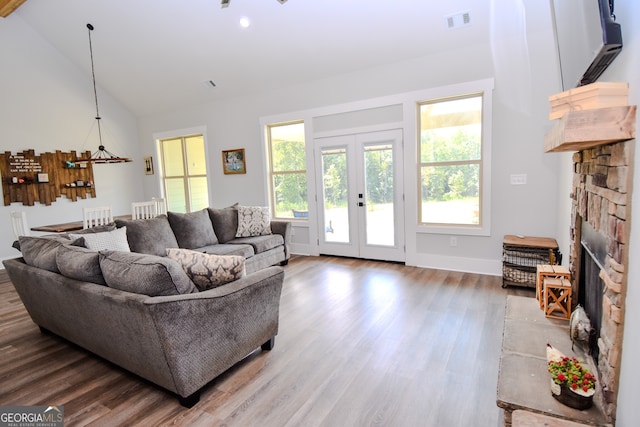 living room with high vaulted ceiling, a stone fireplace, wood-type flooring, and french doors