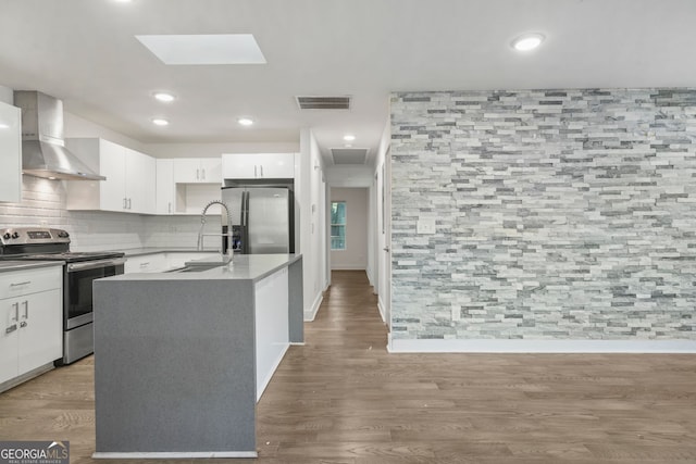 kitchen featuring hardwood / wood-style floors, stainless steel appliances, an island with sink, wall chimney exhaust hood, and white cabinets