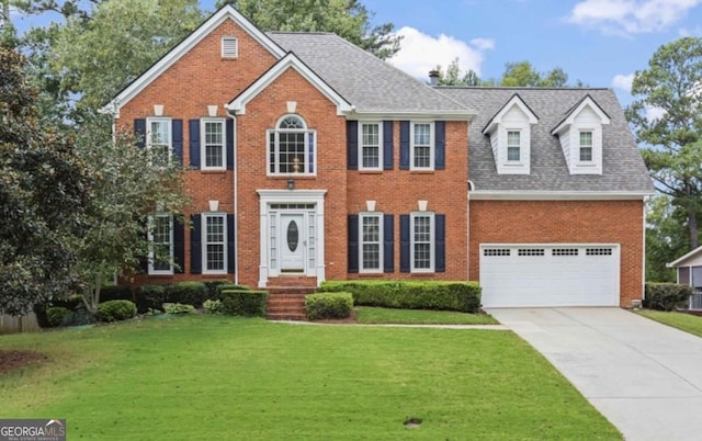 colonial home with a garage, a shingled roof, concrete driveway, a front lawn, and brick siding