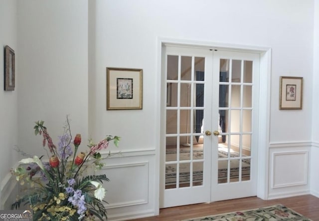 entryway with french doors, wainscoting, a decorative wall, and wood finished floors