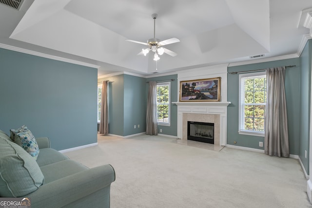 carpeted living room with ceiling fan, a tile fireplace, a raised ceiling, and ornamental molding