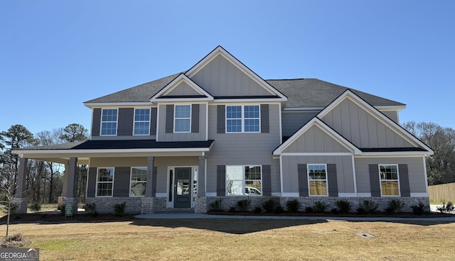 craftsman house with board and batten siding, a front yard, covered porch, and brick siding