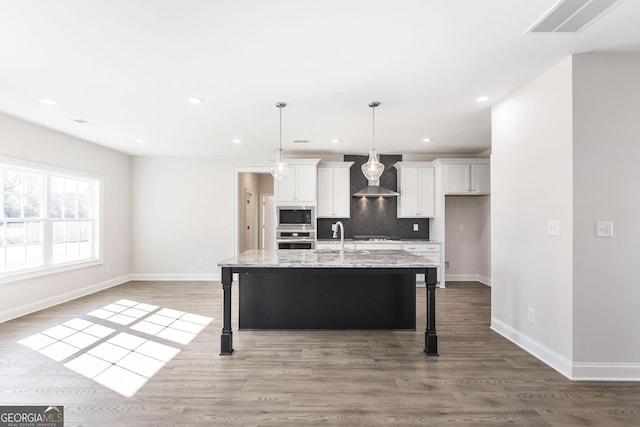 kitchen featuring a breakfast bar, stainless steel appliances, backsplash, white cabinetry, and wall chimney range hood