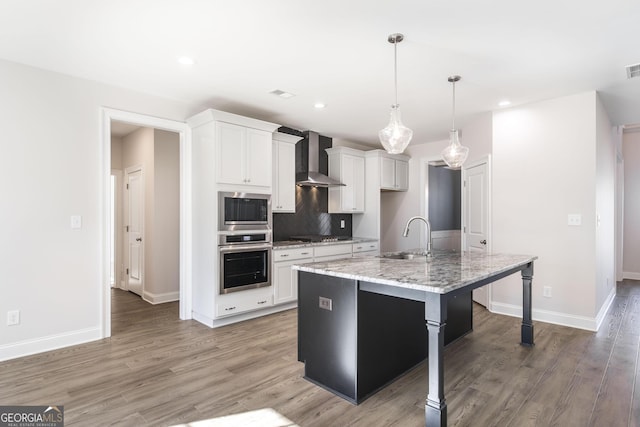 kitchen featuring a center island with sink, stainless steel appliances, white cabinetry, a sink, and wall chimney range hood