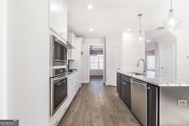 kitchen with light wood finished floors, stainless steel appliances, a kitchen island with sink, white cabinetry, and a sink