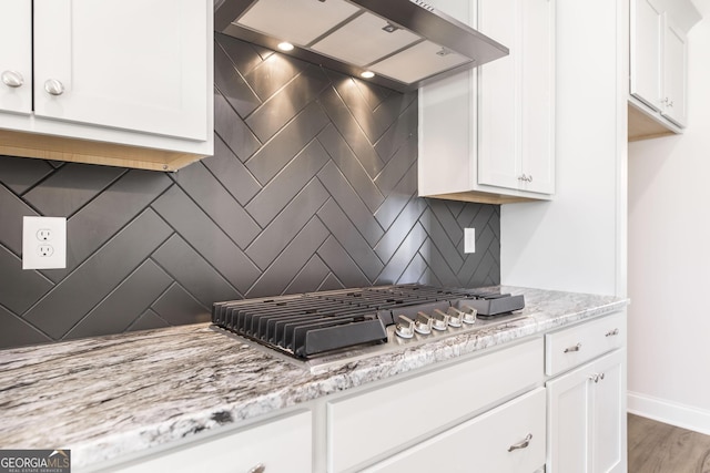 kitchen featuring stainless steel gas cooktop, tasteful backsplash, white cabinetry, wall chimney range hood, and light stone countertops