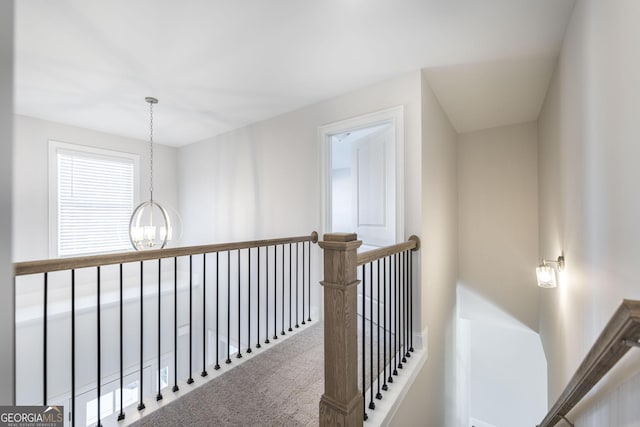 hall with carpet floors, a notable chandelier, and an upstairs landing