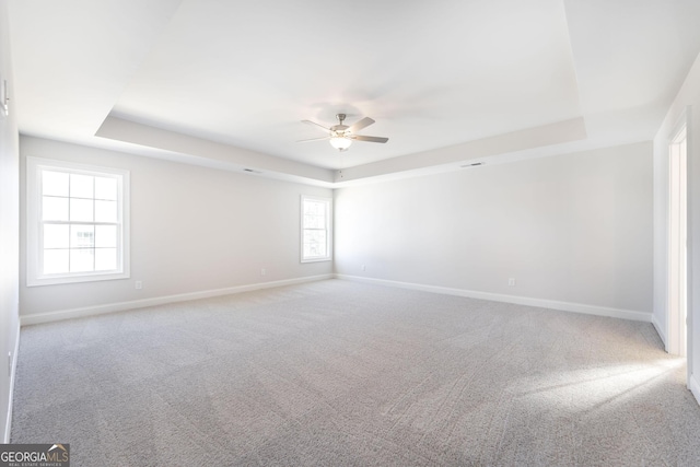 unfurnished room featuring baseboards, a tray ceiling, ceiling fan, and light colored carpet