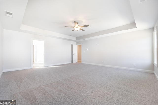 spare room with carpet floors, a tray ceiling, and baseboards