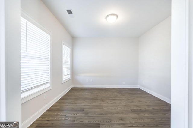 empty room featuring dark wood-style floors, visible vents, and baseboards