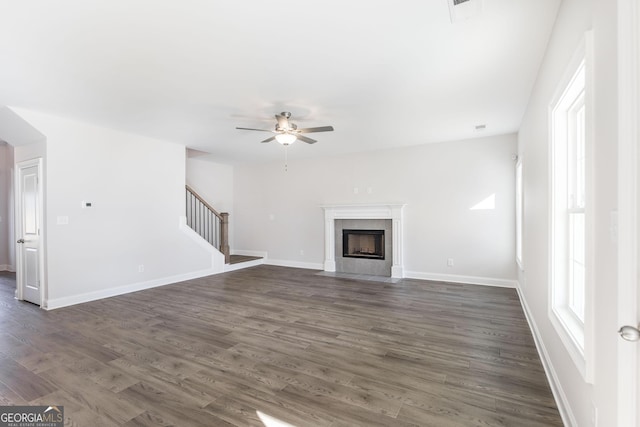 unfurnished living room with dark wood-type flooring, stairway, a fireplace with flush hearth, and a healthy amount of sunlight