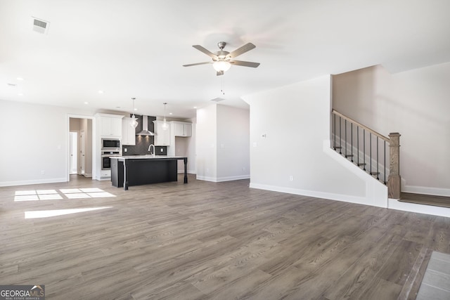 unfurnished living room featuring visible vents, stairway, baseboards, and wood finished floors