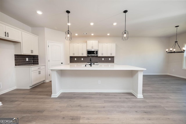 kitchen featuring white cabinetry, hanging light fixtures, stainless steel appliances, an island with sink, and light hardwood / wood-style floors