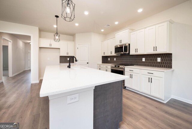 kitchen featuring white cabinets, appliances with stainless steel finishes, a kitchen island with sink, and sink