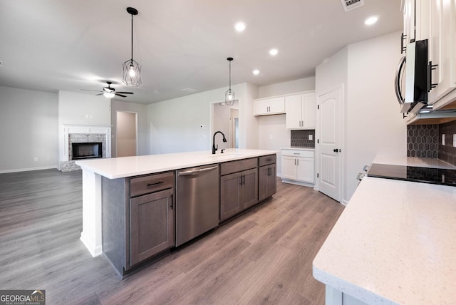 kitchen with hardwood / wood-style floors, white cabinets, a center island with sink, appliances with stainless steel finishes, and tasteful backsplash