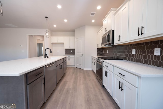 kitchen featuring stainless steel appliances, a kitchen island with sink, light hardwood / wood-style flooring, white cabinetry, and hanging light fixtures