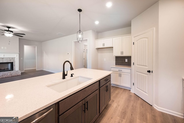 kitchen with pendant lighting, sink, light hardwood / wood-style flooring, a fireplace, and white cabinetry