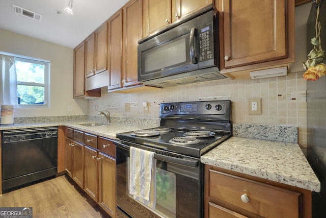 kitchen with light stone counters, light hardwood / wood-style floors, sink, and black appliances