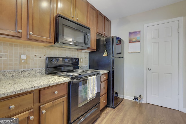 kitchen with black appliances, backsplash, light stone countertops, and light hardwood / wood-style flooring