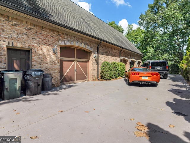 view of property exterior featuring a garage, driveway, brick siding, and roof with shingles