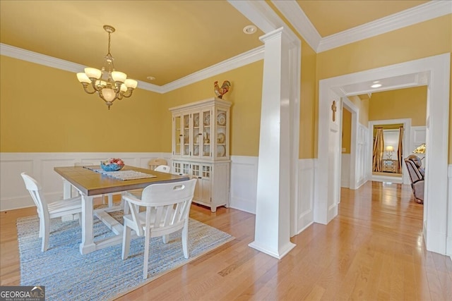 dining room featuring light wood-type flooring, a notable chandelier, decorative columns, and crown molding