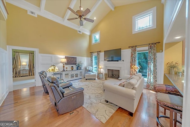 living room with beamed ceiling, a high ceiling, ceiling fan, and light hardwood / wood-style floors