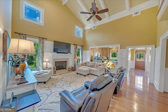 living room with beamed ceiling, high vaulted ceiling, ceiling fan, and light hardwood / wood-style floors