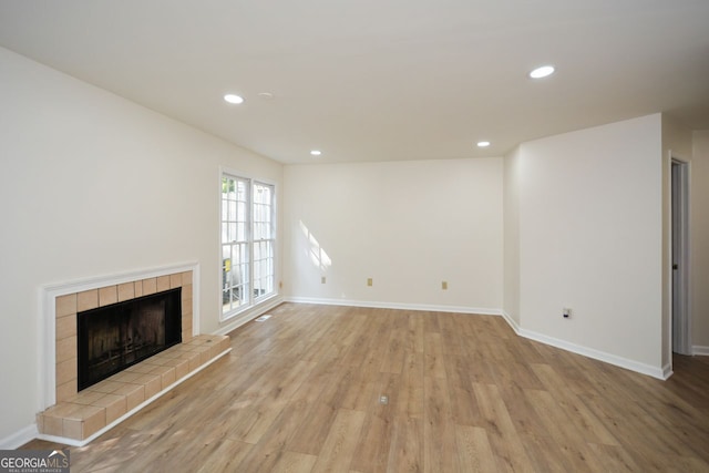 unfurnished living room with a tiled fireplace and light wood-type flooring