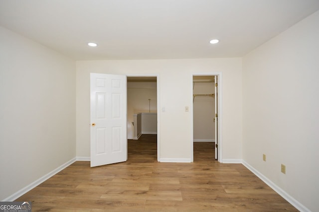 unfurnished bedroom with a closet, a spacious closet, and light hardwood / wood-style floors