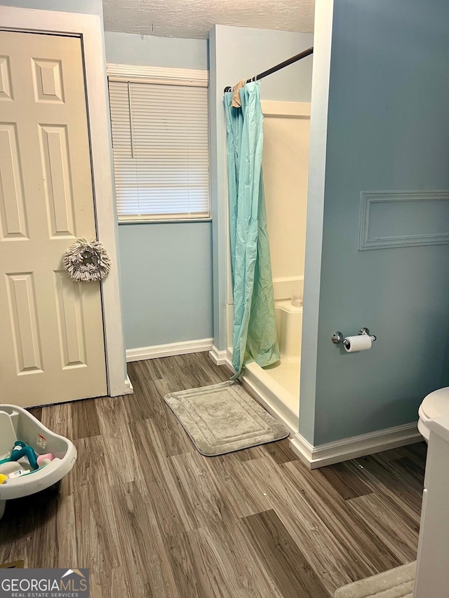 bathroom featuring toilet, baseboards, wood finished floors, and a shower with shower curtain