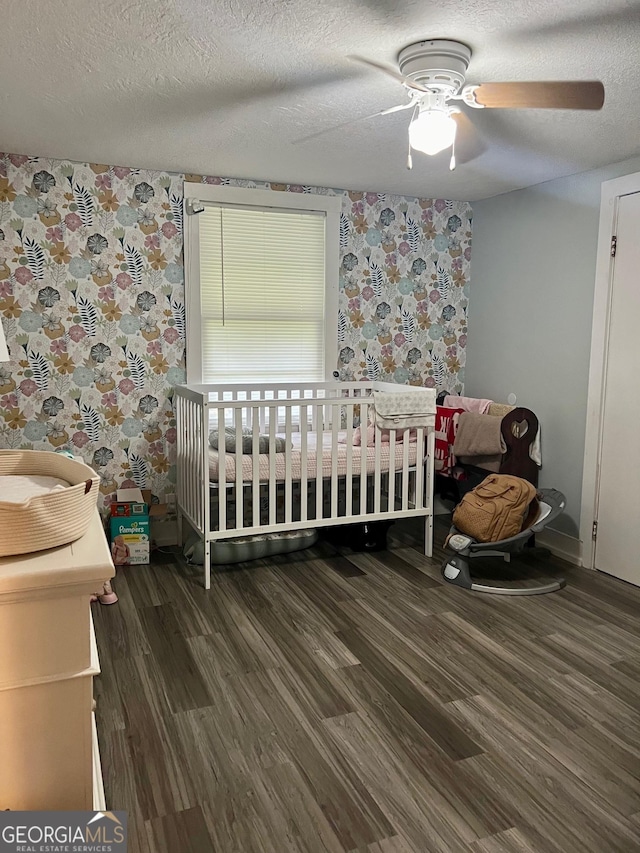 bedroom featuring a nursery area, ceiling fan, a textured ceiling, and wood finished floors