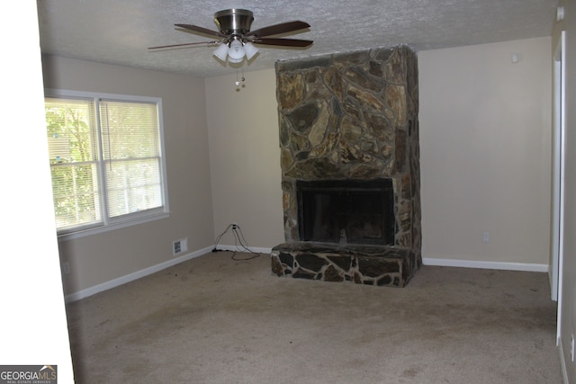 unfurnished living room with carpet flooring, ceiling fan, a textured ceiling, and a stone fireplace