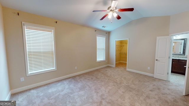 unfurnished bedroom with light carpet, a closet, baseboards, a spacious closet, and vaulted ceiling